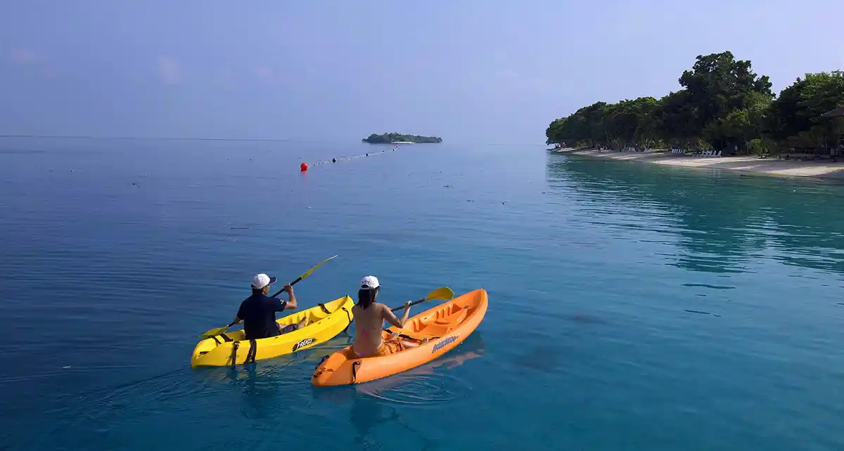 Couple enjoying a peaceful paddle in a sea kayak on the crystal-clear turquoise ocean in front of Pom Pom Island resort in the Tun Sakaran Marine Park near Semporna
