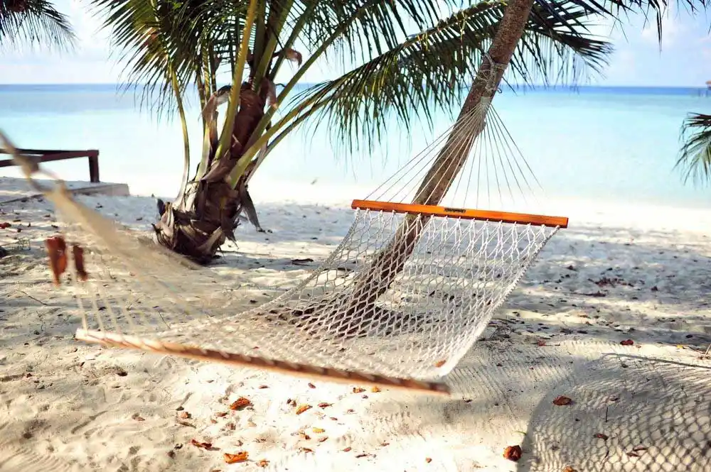 A relaxing hammock strung between two palm trees on a pristine white sand beach of Mabul island, the perfect spot for an afternoon nap in paradise.